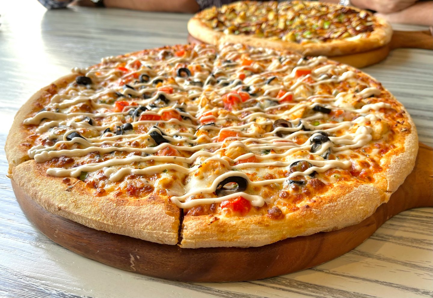 Dua pizza segar yang baru dipanggang di atas talenan kayu di atas meja.